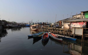 Boats neatly arranged and docked in the slums with pinisi boats docked in Sunda Kelapa Port in the background.