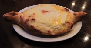 Adjaruli Khachapuri with a raw egg peeking through the cheese and butter in the middle.